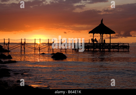 Tramonto d'oro e sagome - due persone su un piccolo e romantico jetty, guardare il sole andare giù con riflessioni sull'oceano. Foto Stock