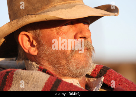 Un vecchio cowboy timer appoggiata contro il suo pack e la sella al tramonto Foto Stock