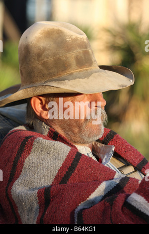 Un vecchio cowboy timer appoggiata contro il suo pack e la sella accanto alla Chuck wagon al tramonto Foto Stock