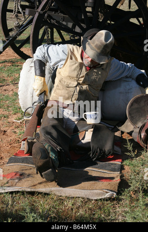 Un vecchio cowboy timer appoggiata contro il suo pack e la sella accanto alla Chuck wagon per raggiungere il suo fucile Foto Stock