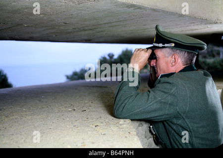 Un attore vestito come un ufficiale tedesco che si affaccia sul canale in lingua inglese e da un tedesco D giorno bunker in Normandia Francia Foto Stock