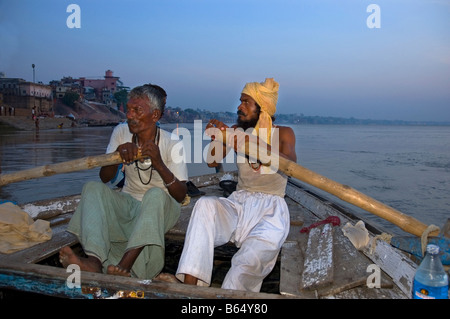 I battellieri riga barca turistica durante la mattina presto tour dei ghats lungo il fiume Gange a Varanasi India Foto Stock