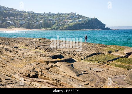 L'uomo la pesca nel Mare di Tasman mentre stava su rocce adiacente alla spiaggia di balene,sydney, Australia, shot è guardando verso nord Foto Stock