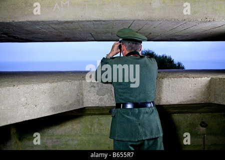 Un attore vestito come un ufficiale tedesco che si affaccia sul canale in lingua inglese e da un tedesco D giorno bunker in Normandia Francia Foto Stock