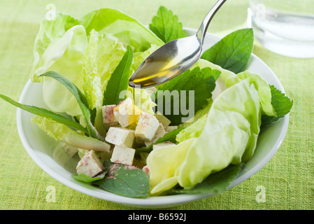 Cucchiaio drizzling olio d'oliva su insalata di verdure miste e i cubetti di tofu Foto Stock