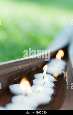 Acceso candele votive galleggianti in acqua entro a tazza di foglie di palma Foto Stock