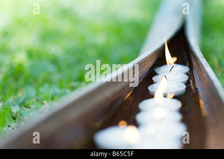 Acceso candele votive galleggianti in acqua in foglia di palma Foto Stock