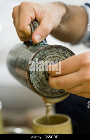 Le mani versando il tè in tazza Foto Stock