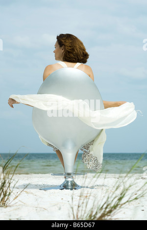 Donna seduta nella sedia sulla spiaggia, guardando a vista, sciarpa soffia nella brezza Foto Stock