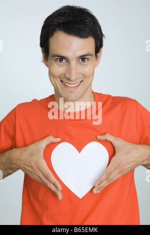 Man mano intorno al cuore simbolo stampato sulla sua maglietta, sorridente in telecamera Foto Stock