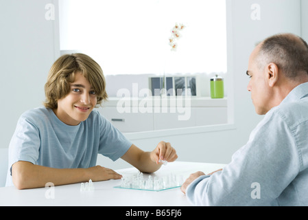 Teen boy giocando a scacchi con padre, sorridente in telecamera Foto Stock