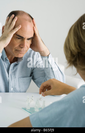 Padre e figlio giocare a scacchi, man tenendo la testa con entrambe le mani Foto Stock