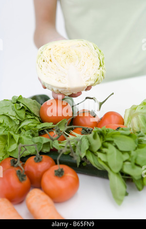 Mano che tiene la metà testa di lattuga, un assortimento di verdure fresche in primo piano Foto Stock
