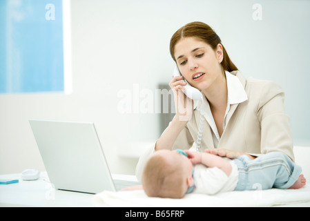 Professional donna toccando bambino giacente sulla scrivania, rendendo chiamata telefonica Foto Stock