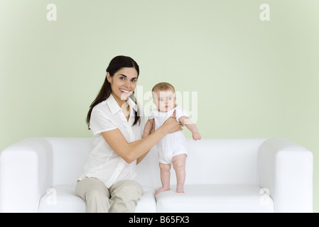 Donna aiutando baby stand sul lettino, sorridente in telecamera Foto Stock