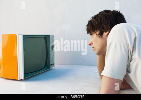 Giovane uomo appoggiata sul gomito, guardare la televisione Foto Stock