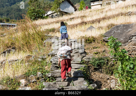 I bambini piccoli salendo un percorso sul lato dei modi valle fluviale nella catena Hannapurna in Himalaya, Nepal Foto Stock