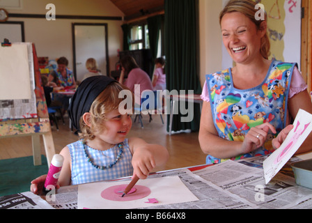 Bambina incollaggio una foto nella nursery con un insegnante Foto Stock