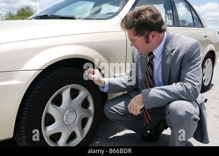 Un uomo di affari sulla strada con un pneumatico flate ha appena scoperto la vite che ha causato il pneumatico per andare flat Foto Stock