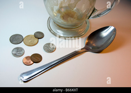 Vuoto in vetro Cappuccino, un cucchiaio di metallo su una superficie bianca con le monete degli Stati Uniti; 2 spiccioli, 2 nickels, 1, dime 1 trimestre, 1 dollaro moneta Foto Stock