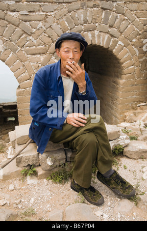 Uomo senior di fumare su una parete, la Grande Muraglia Cinese a Pechino, Cina Foto Stock