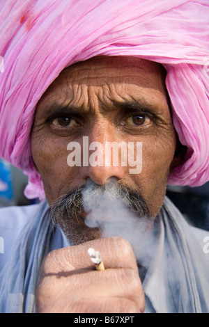 Ritratto di un uomo indiano con fumo proveniente dal naso, indossando un turbante rosa, fumare una bidi a Jaipur, India Foto Stock