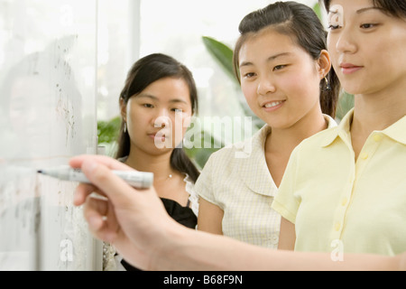 Persona della scrittura a mano su una lavagna con tre donne lavoratori ufficio sta guardando Foto Stock