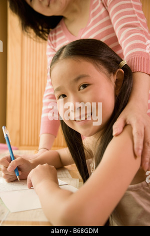 Profilo laterale di una ragazza con una penna con sua madre in piedi accanto a lei Foto Stock