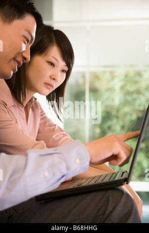 Profilo laterale di un giovane uomo seduto accanto a una giovane donna e puntare il dito sullo schermo di un computer portatile Foto Stock