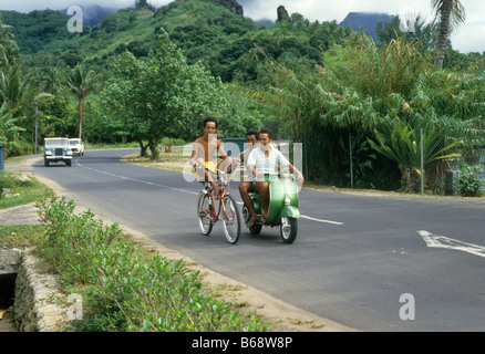 Teen boy sulla bici tirato da altri ragazzi su scooter Sud Pacifico , Moorea, Tahiti Foto Stock