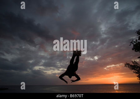 Giamaica Negril Silhouette di un giovane uomo che saltava dalla rupe sopra la grotta dei pirati Foto Stock