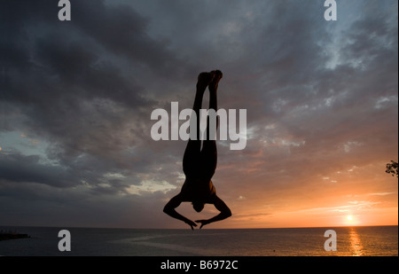 Giamaica Negril Silhouette di un giovane uomo che saltava dalla rupe sopra la grotta dei pirati Foto Stock