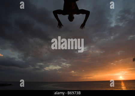 Giamaica Negril Silhouette di un giovane uomo che saltava dalla rupe sopra la grotta dei pirati Foto Stock