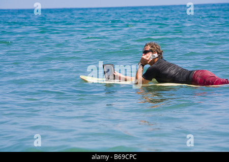 Uomo che parla su un telefono e utilizzando un computer portatile in mare Foto Stock