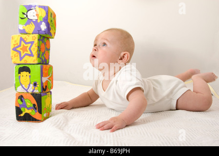 Baby Boy cercando fino ad una pila di mattoni giocattolo tagliati su bianco Foto Stock