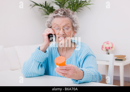 Senior donna pillola tenendo la bottiglia e parlando al telefono Foto Stock