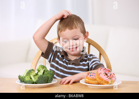 Giovane ragazzo che la scelta tra i broccoli e ciambelle Foto Stock