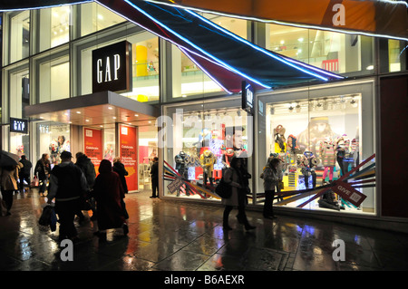 I clienti bagnati fuori dal negozio di moda Gap e dal negozio Window Oxford Street London West End di notte gente Natale Shopping nella pioggia Inghilterra Regno Unito Foto Stock