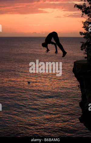 Giamaica Negril Silhouette di un giovane uomo che saltava dalla rupe sopra la grotta dei pirati Foto Stock