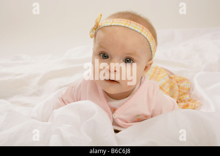 A sei mesi il bambino giacente sul suo fronte su tessuto bianco vestito in rosa e abiti di colore giallo Foto Stock