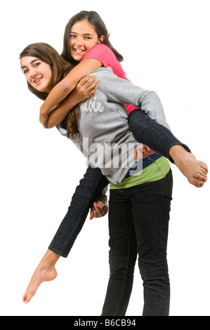 Chiudere verticale su ritratto di due ragazze adolescenti uno di dare agli altri un piggy back ride contro uno sfondo bianco. Foto Stock