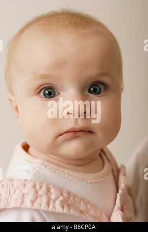 A sei mesi Baby girl guardando dritto verso la lente della fotocamera con un espressione triste Foto Stock