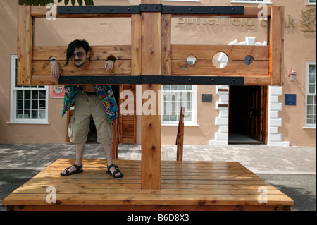 Giovane uomo pone in una replica gogna nella storica King's Square, St George, Bermuda Foto Stock