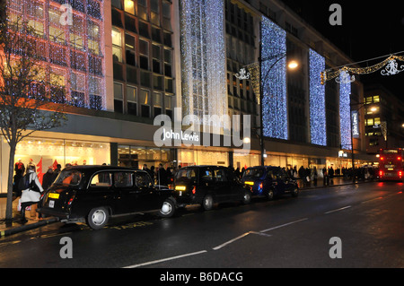 John Lewis grandi magazzini London West End Oxford Street con luci natalizie e taxi che raccolgono e rilasciano gli acquirenti Inghilterra Regno Unito Foto Stock