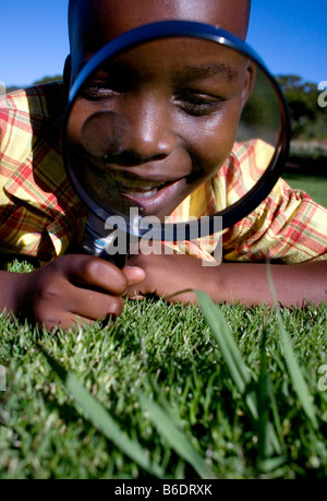 Boy utilizzando una lente di ingrandimento per esaminare un'area d'erba. Foto Stock