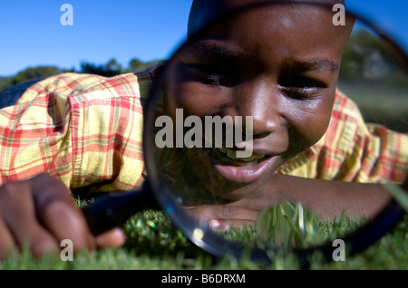 Boy utilizzando una lente di ingrandimento per esaminare un'area d'erba. Foto Stock