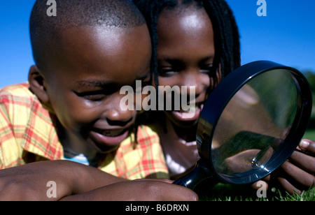 I bambini utilizzando una lente di ingrandimento per esaminare un'area d'erba. Foto Stock