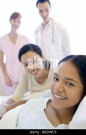 Adolescente paziente in ospedale. Medico e infermiere in piedi da un paziente e sua madre. Foto Stock