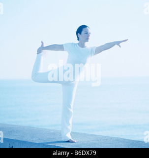 Donna in piedi in posizione di yoga con una delle sue gambe inclinate dietro di lei. Foto Stock