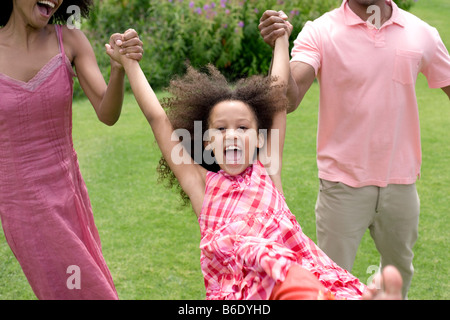 La famiglia felice. I genitori oscillare la loro figlia in un giardino. Foto Stock